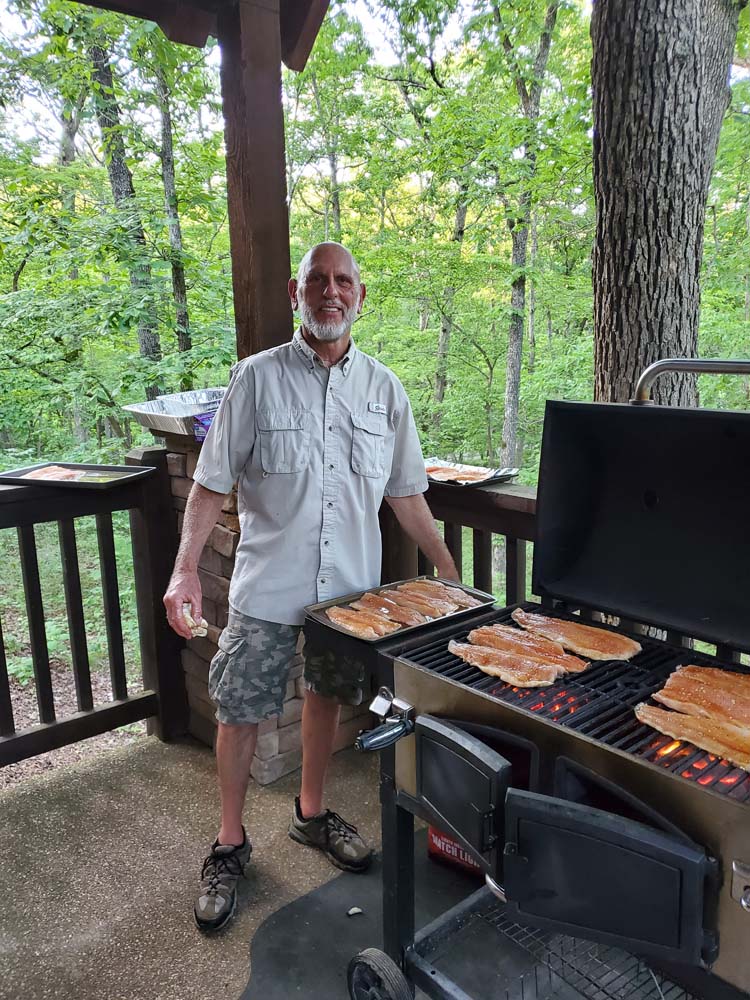 Man with Legacy Builders standing next to a grill cooking fish