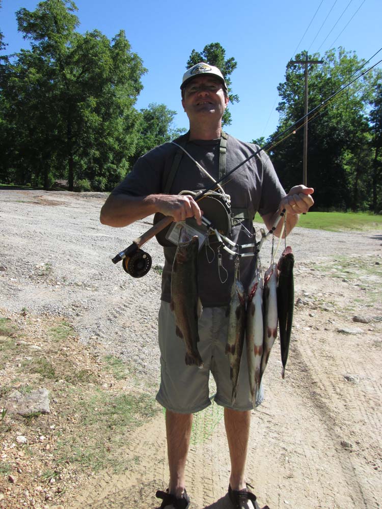Man with Legacy Builders standing in a dirt road holding up a string of fish caught