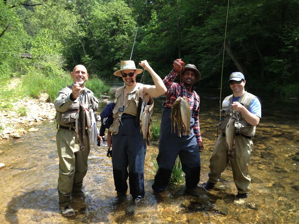 Four men with Legacy Builders standing in a creek each holding up a string of fish caught