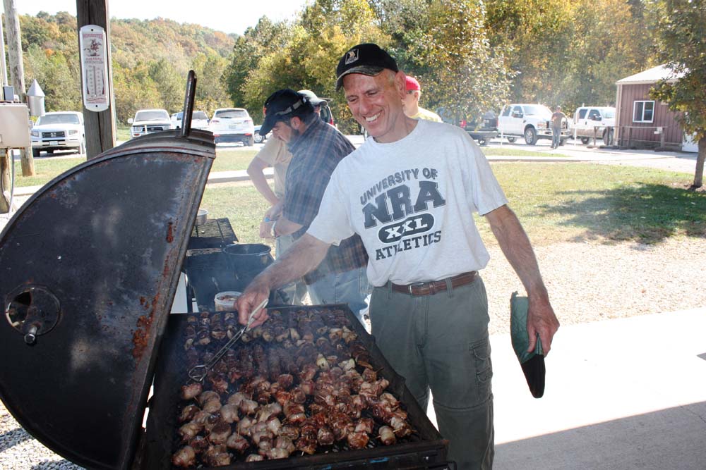 Man smiling while turning meat on the grill at Legacy Builders fall retreat